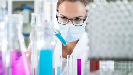 Eine Wissenschaftlerin arbeitet im Labor und trägt dabei eine Schutzmaske.