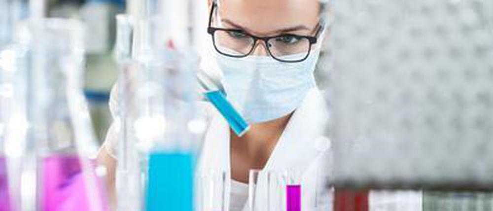 Eine Wissenschaftlerin arbeitet im Labor und trägt dabei eine Schutzmaske.