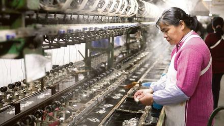 Eine Arbeiterin steht in einer chinesischen Seidenfabrik an einer Maschine, an der Seidenfäden gewonnen werden.