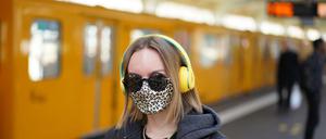 Junge Frau mit Mund-Nase-Bedeckung und Kopfhörer in einem U-Bahnhof in Berlin.