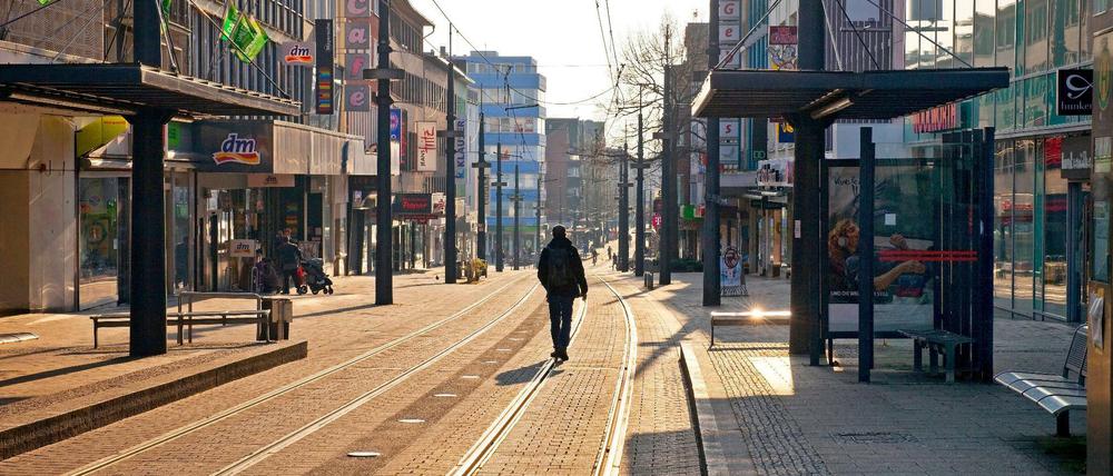 Ein Mann geht durch eine menschleere Fußgängerzone mit Straßenbahngleisen.