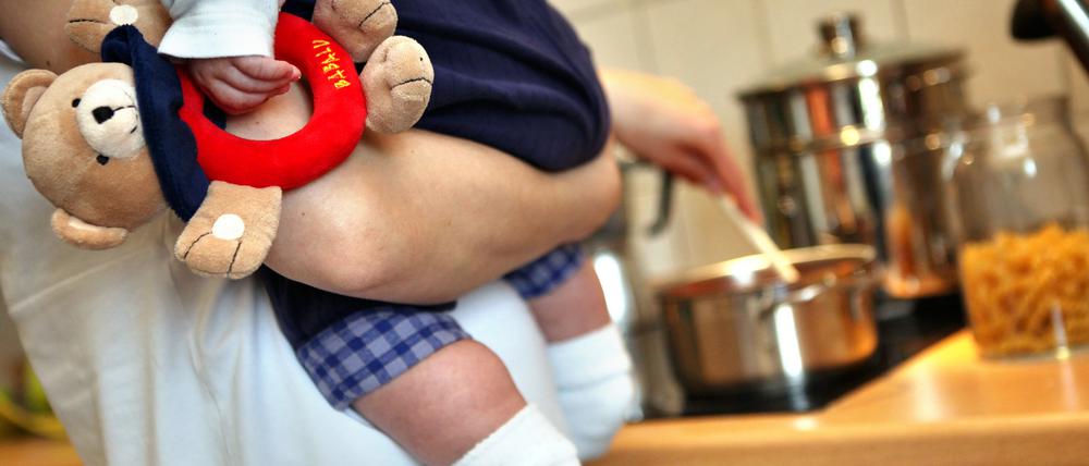 Eine Mutter hält beim Kochen ihr Kleinkind auf dem Arm.
