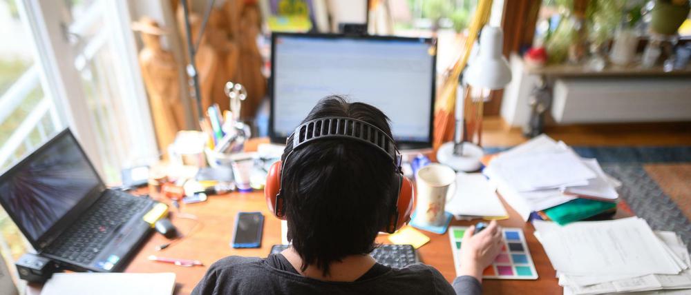 Eine Frau arbeitet mit Hörschutz an einem Schreibtisch mit Laptop und Desktop im Homeoffice.