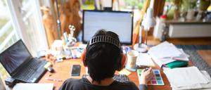 Eine Frau arbeitet mit Hörschutz an einem Schreibtisch mit Laptop und Desktop im Homeoffice.