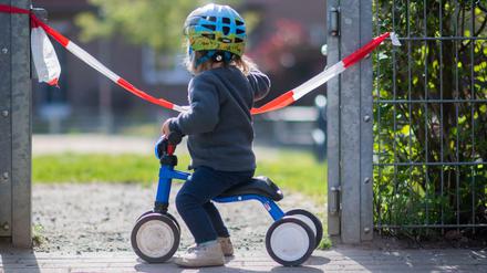 Ein kleines Mädchen steht vor einem gesperrten Spielplatz.