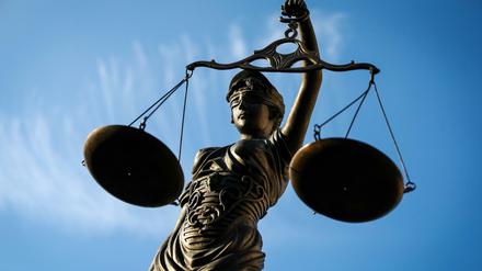 Eine Justitia-Statute, die eine Waage in der Hand hält, ist schräg von unten gegen den blauen Himmel fotografiert.