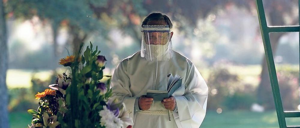 Das Virus verändert die Trauer. Ein Priester mit Gesichtsschutz bei der Beerdigung eines Corona-Patienten. Foto: