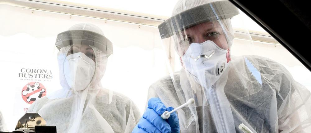 Mitarbeiter vom Gesundheitsamt in Mitte halten ein Abstrichstäbchen in ein Autofenster auf dem zentralen Festplatz in der ambulanten Corona-Test- Einrichtung.