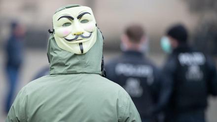 Eine Frau mit einer Guy-Fawkes-Maske steht hinter Polizisten. Zuvor hatten die sogenannten "Corona-Rebellen" im Internet zu einer Demonstration aufgerufen.