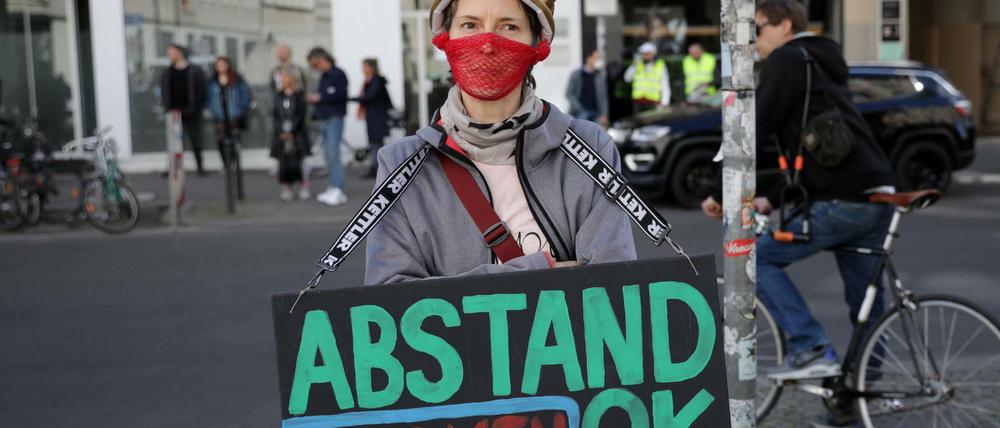 Eine Demonstrantin mit selbst gebautem Mundschutz und einer Plastikkrone steht am Rande einer Demonstration am Rosa-Luxemburg-Platz.