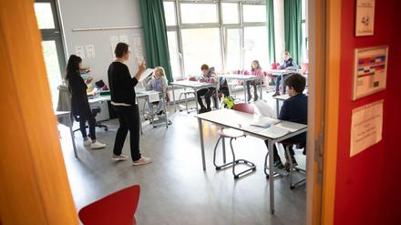 Eine Grundschullehrerin und eine angehende Lehrkraft erklären einer Grundschulklasse die Abstandsregeln.