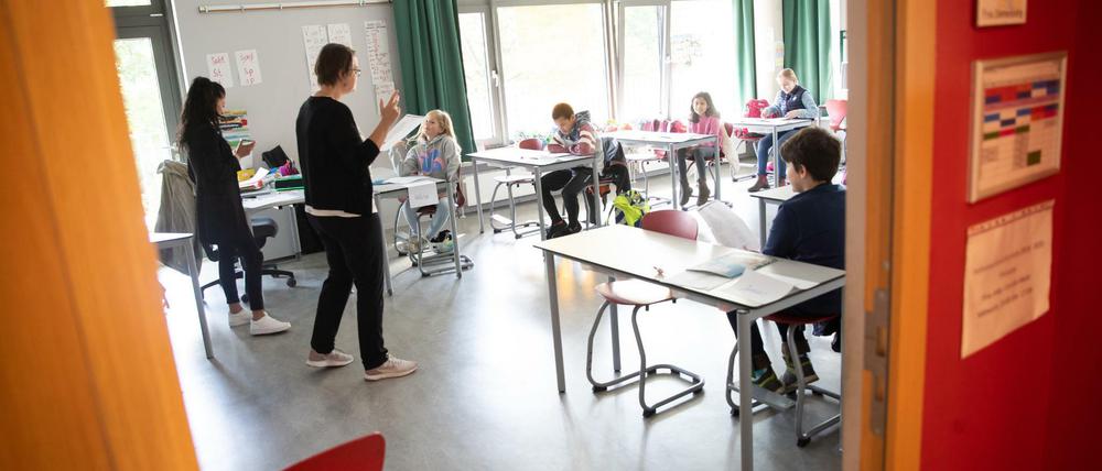 Eine Grundschullehrerin und eine angehende Lehrkraft erklären einer Grundschulklasse die Abstandsregeln.