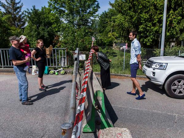 Vor und hinter einer Grenzschranke stehen Menschen und lächeln sich zu.