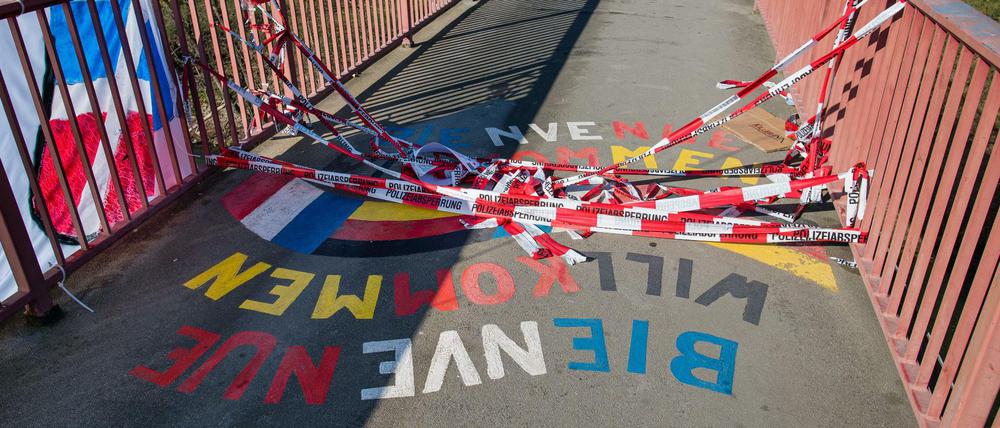 Auf einer Brücke liegt rot-weißes Absperrband auf dem Schriftzug Willkommen, Bienvenue.