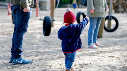 Ein Kind steht mit seinen Eltern auf einem Spielplatz.