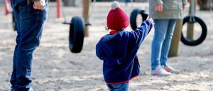 Ein Kind steht mit seinen Eltern auf einem Spielplatz.