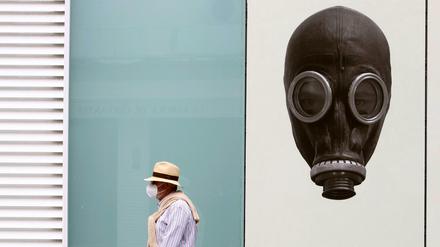 Straßenszene im spanischen Málaga: Ein Mann mit Mundschutz vor dem Bild einer Person mit Gasmaske