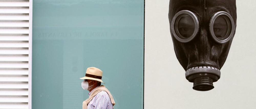 Straßenszene im spanischen Málaga: Ein Mann mit Mundschutz vor dem Bild einer Person mit Gasmaske