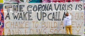 Im Münchner Schlachthofviertel schreibt ein Kunststudent ein Graffito auf eine Wand - mit dem Text: The corona virus is a wake up call and our chance to build a new and loving society.