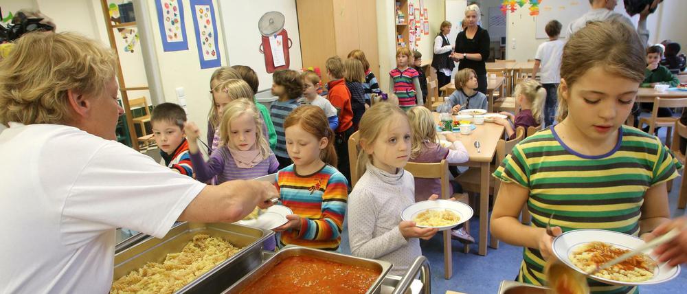 Schülerinnen und Schüler werden in der Mensa einer Grundschule mit Nudeln und Tomatensoße bedient.