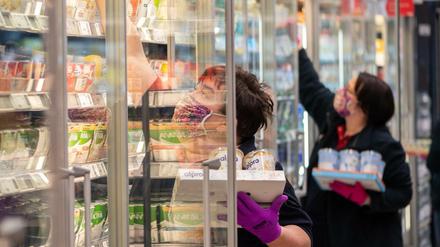 Mitarbeiterinnen in einem Supermarkt tragen Schutzmasken, während sie Regale mit Waren bestücken (Symbolbild).