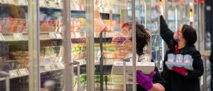 Mitarbeiterinnen in einem Supermarkt tragen Schutzmasken, während sie Regale mit Waren bestücken (Symbolbild).