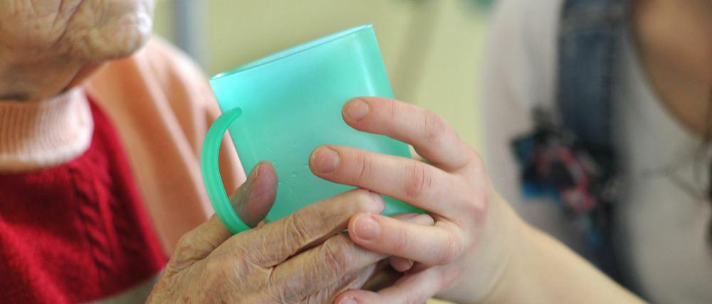 Eine Pflegekraft hilft einer alten Frau in Frankfurt (Oder) beim Trinken aus einem Becher in einem Seniorenheim.