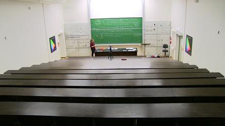 In einem Hörsaal steht eine Dozentin erklärend vor einer Tafel mit Formel, dabei wird sie gefilmt.
