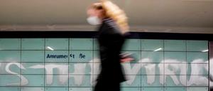 Eine Frau mit Mund-Nasen-Schutz geht am U-Bahnhof Amrumer Straße in Berlin an einem Graffiti vorbei.