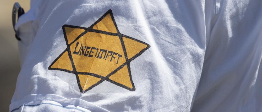 "Ungeimpft" steht auf einem nachgebildeten "Judenstern" am Arm eines Mannes auf einer Demonstration.