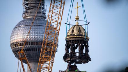  Ein Kran hebt am Neubau vom Berliner Schloss die Kuppelspitze mit einem Kreuz auf die Kuppel.
