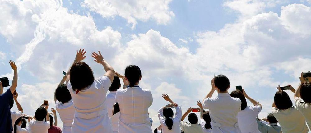 Medizinisches Personal des Zentralkrankenhauses der Selbstverteidigungskräfte stehen und winken, während die Kunstflugstaffel der japanischen Selbstverteidigungsstreitkräfte am Himmel über Tokio fliegt.