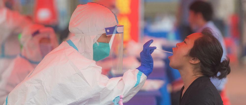 China, Wuhan: Ein Mitarbeiter des Gesundheitswesen entnimmt eine Rachenprobe für einen Corona-Test bei einer jungen Frau in einer Grundschule im Bezirk Dongxihu.