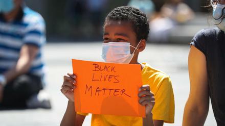 Ein Junge mit Mundschutz hält während einer Demonstration ein Plakat mit der Aufschrift «Black lives matter» in der Hand.