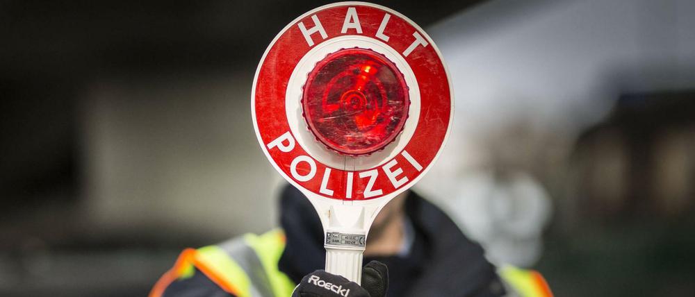 Ein Polizeibeamter hält eine Polizeikelle im Rahmen einer Verkehrskontrolle hoch.
