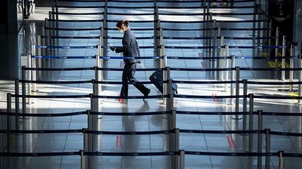 Düsseldorf: Eine Frau mit Mundschutz geht in einem geisterhaften Flughafen-Terminal zu einem Check In-Schalter.