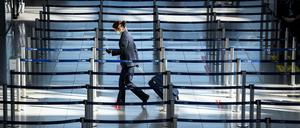 Düsseldorf: Eine Frau mit Mundschutz geht in einem geisterhaften Flughafen-Terminal zu einem Check In-Schalter.