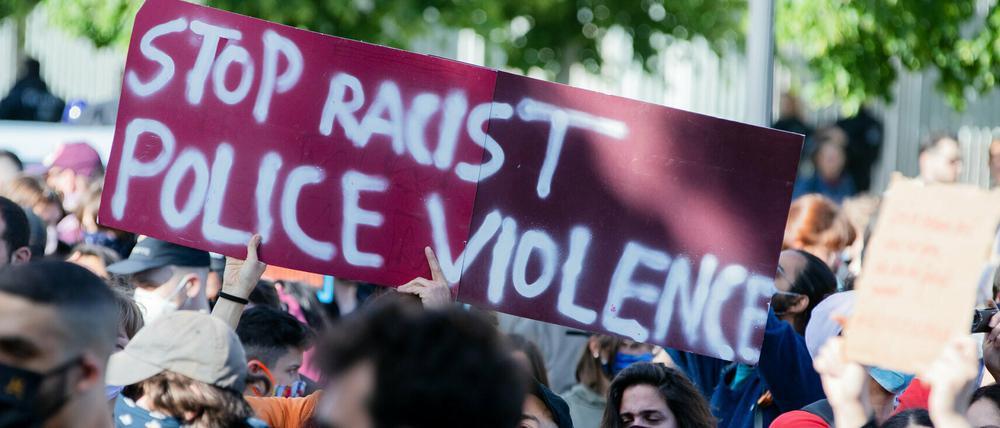 Teilnehmende einer Kundgebung in Berlin halten ein Plakat mit der Aufschrift: "Rassistische Polizeigewalt stoppen".