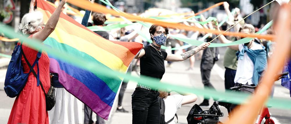 Teilnehmer der "Unteilbar"-Demo stehen mit Mundschutz und einer Regenbogenfahne nahe dem Brandenburger Tor.