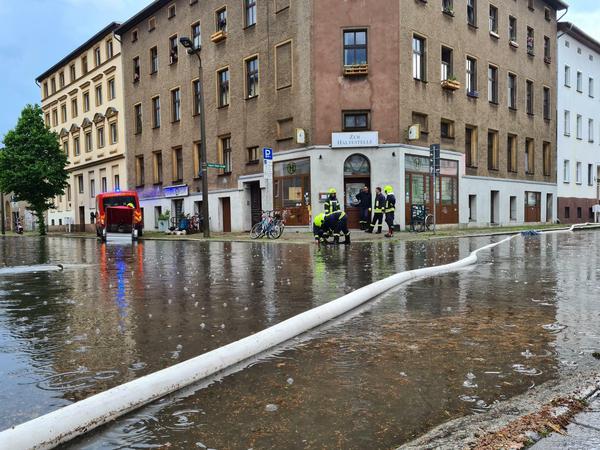 Mit Schläuchen pumpt die Feuerwehr nach einem Unwetter mit Starkregen Wasser von einer Straße.