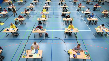 Abiturienten schreiben ihre Klausuren an weit auseinander stehenden Tischen in einer Turnhalle.