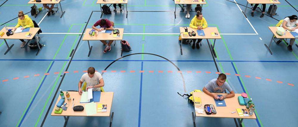 Abiturienten schreiben ihre Klausuren an weit auseinander stehenden Tischen in einer Turnhalle.