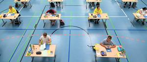 Abiturienten schreiben ihre Klausuren an weit auseinander stehenden Tischen in einer Turnhalle.