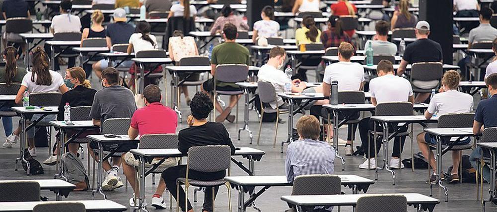 Studierende sitzen bei einer Prüfung in einer Messehalle an Einzeltischen.