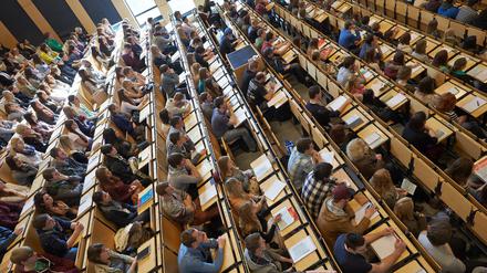 Studierende sitzen in einem von der Seite beleuchteten Hörsaal und lauschen einer Lehrveranstaltung.