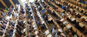 Studierende sitzen in einem von der Seite beleuchteten Hörsaal und lauschen einer Lehrveranstaltung.