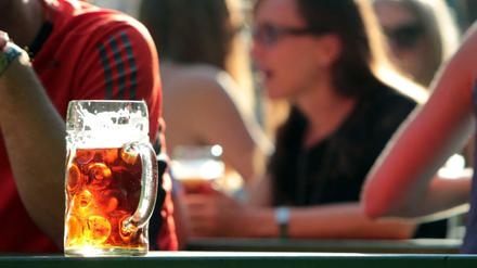 Bierglas auf Bierbank vor Menschen im Biergarten.
