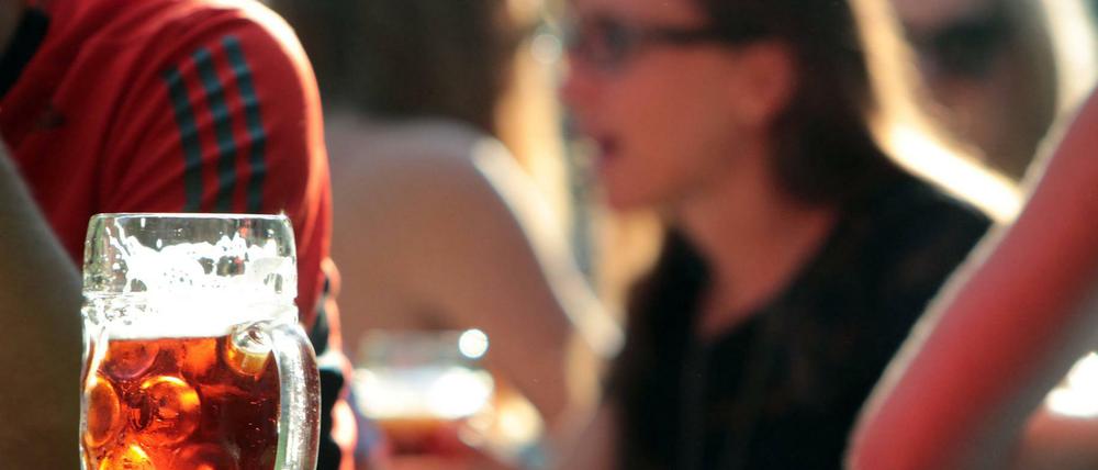 Bierglas auf Bierbank vor Menschen im Biergarten.