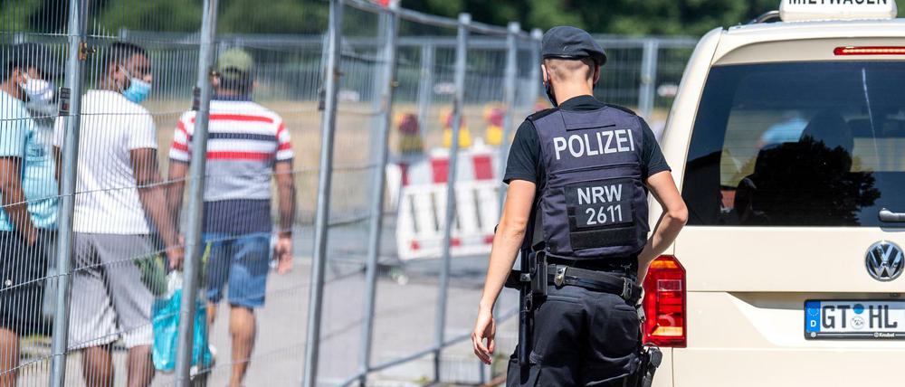 Ein Polizist geht zu einer Gruppe von Menschen, die hinter einem Bauzaun unter Quarantäne stehen. Nach dem Corona-Ausbruch beim Fleischverarbeiter Tönnies verhängen die Behörden einen Lockdown auch für den Kreis Gütersloh und den Nachbarkreis.