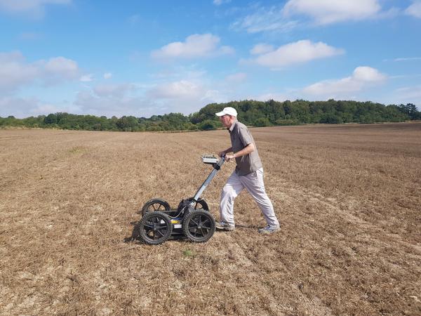 Ein Mann schiebt einen Wagen mit einem Radarscan-Gerät über ein brachliegendes Feld.